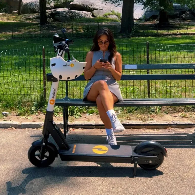 Rider checking the app on a park bench beside a parked iPakket e-scooter