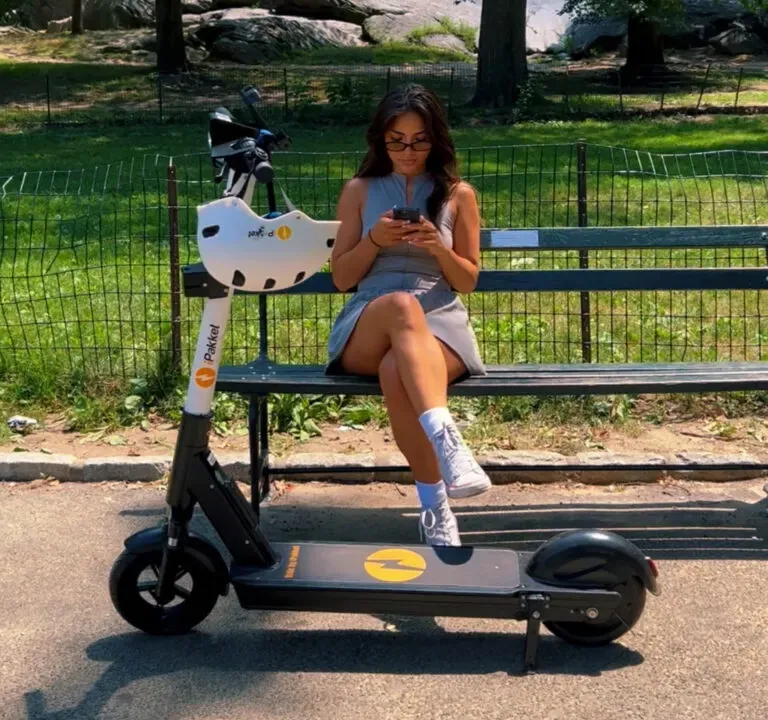 Rider checking the app on a park bench beside a parked iPakket e-scooter