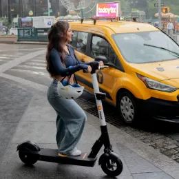 Rider on an iPakket e-scooter beside a yellow cab in the rain