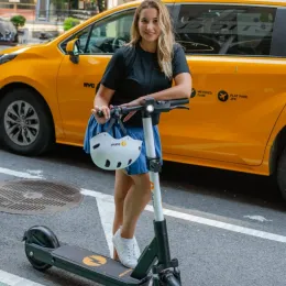 Rider standing with an iPakket e-scooter in front of a yellow cab