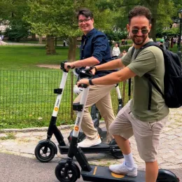 Two riders on iPakket e-scooters on a park path