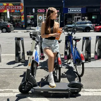 Rider on a Ride by iPakket e-scooter next to a Citi Bike dock in Manhattan