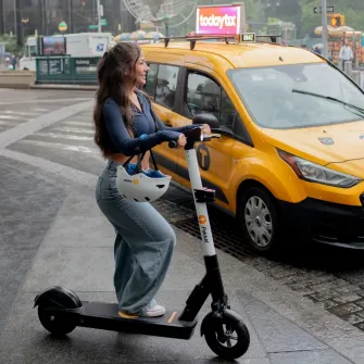 Rider on a Ride by iPakket e-scooter in the rain beside a yellow cab