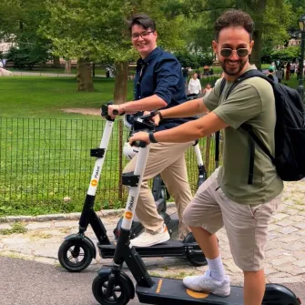 Two riders side by side on Ride by iPakket e-scooters on a park path